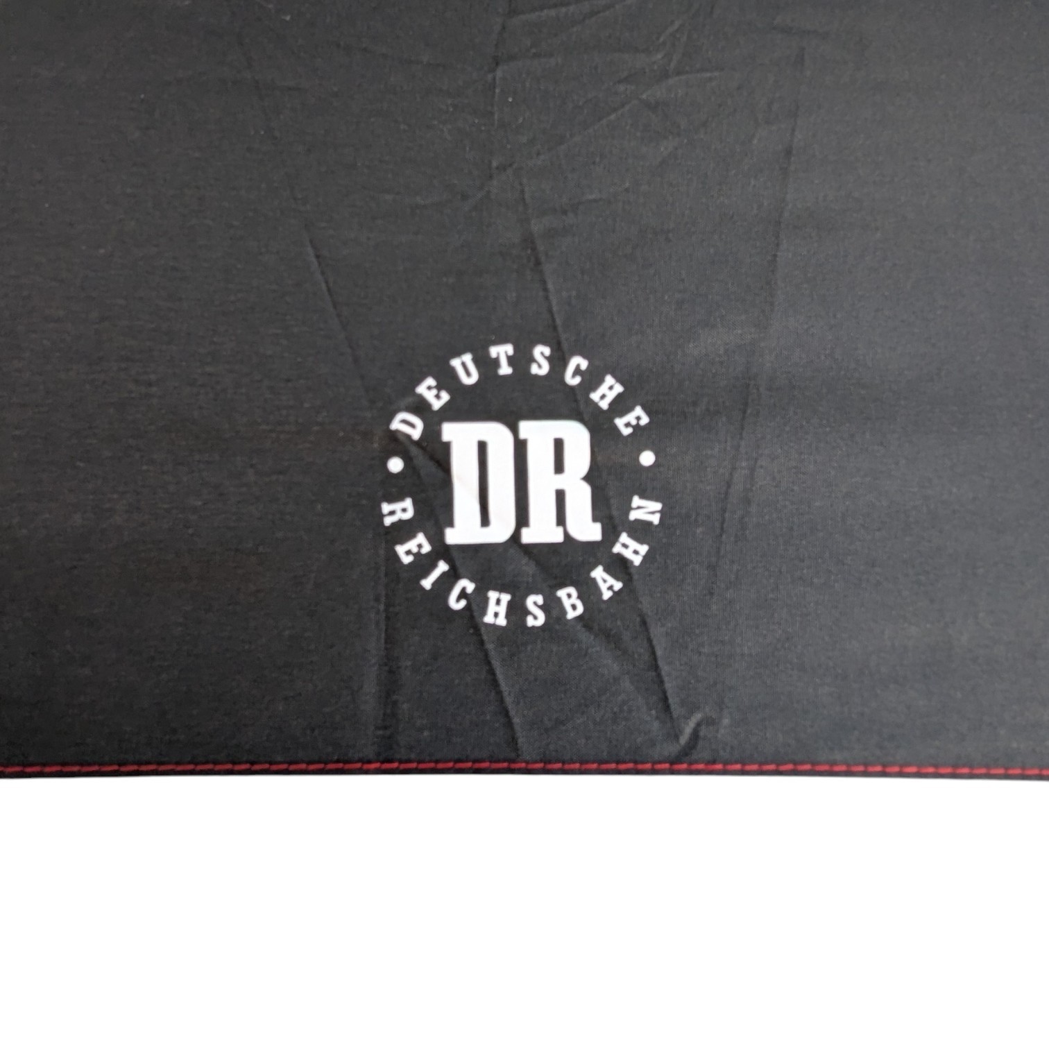 Weißes DR-Logo der Deutschen Reichsbahn auf schwarzem Taschenschirm, Detailansicht